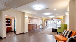 A hotel lobby with a reception desk, a green armchair, and a patterned rug. - Comfort Inn and Suites (Fredericksburg)