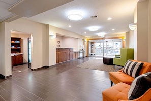 Un hall de hotel con una mesa de recepción, un sillón verde y una alfombra estampada.