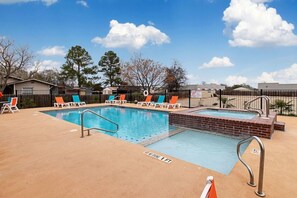 Una piscina con sillones de descanso, terraza de ladrillo y valla.