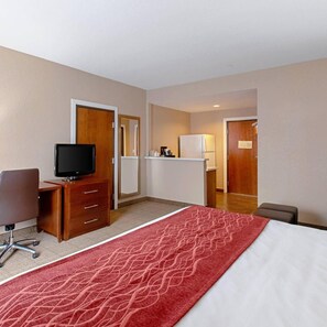 A hotel room with a bed, a desk with a television, a chair, a kitchenette, and a bathroom. - Comfort Inn and Suites (Fredericksburg)