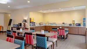 A hotel dining area with multiple tables and chairs, a kitchen counter with appliances, and a large painting on the wall. - Comfort Inn and Suites (Fredericksburg)