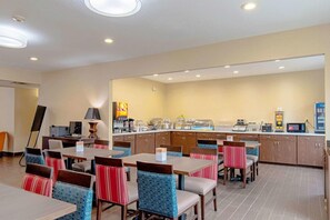 Un comedor de hotel con varias mesas y sillas, una barra de cocina con electrodomésticos y un cuadro grande en la pared.