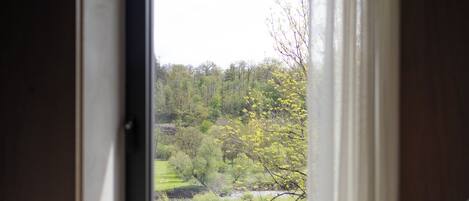 A bedroom with a large window, a bed, and a view of a green landscape with trees and a fence.