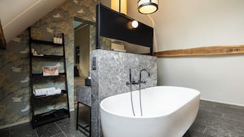 A modern bathroom with a freestanding bathtub, a black shelf unit with toiletries, and a mirror above the tub.