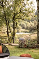 Un jardin avec une clôture en métal, un banc en pierre et une zone herbeuse avec des arbres.