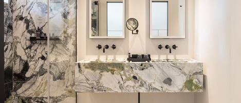 A bathroom with a marble vanity, two mirrors, a showerhead, and a small round mirror on the wall.