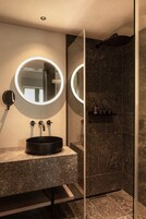 Un baño moderno con un espejo redondo, un lavabo negro y una zona de ducha.