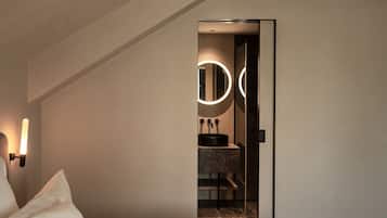 Een moderne hotelkamer met een bed, een badkamer met een ronde spiegel en een klein wastafeltje.