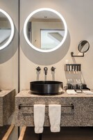 Un baño moderno con un espejo redondo, un lavabo negro y un perchero para toallas.