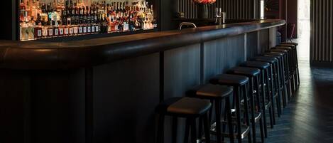 A bar area with a long counter, multiple stools, and a wall-mounted liquor display.