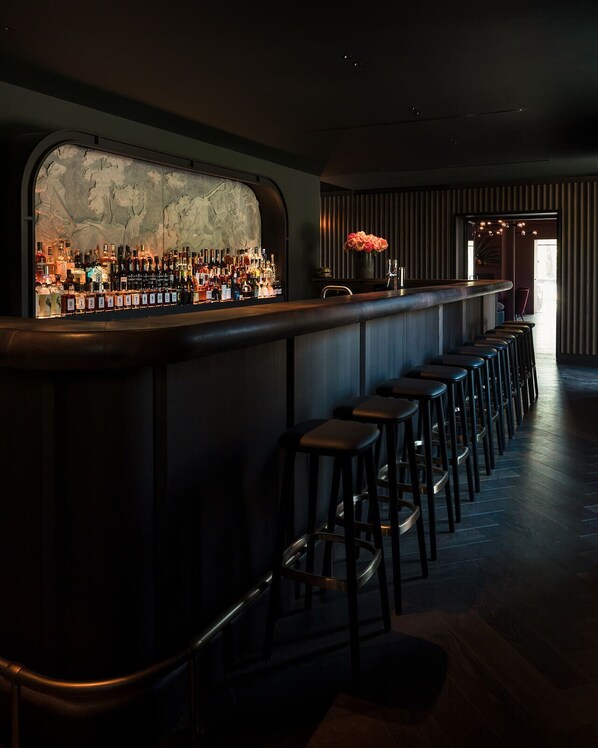 A bar area with a long counter, multiple stools, and a wall-mounted liquor display.
