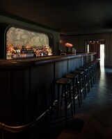 Una zona de bar con una barra larga, varios taburetes y un mostrador mural para licores.