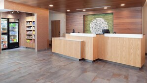 A reception area with a wooden reception desk, a refrigerated beverage display, and a wall-mounted decorative piece. - Fairfield Inn & Suites by Marriott Fort Morgan (Fort Morgan)