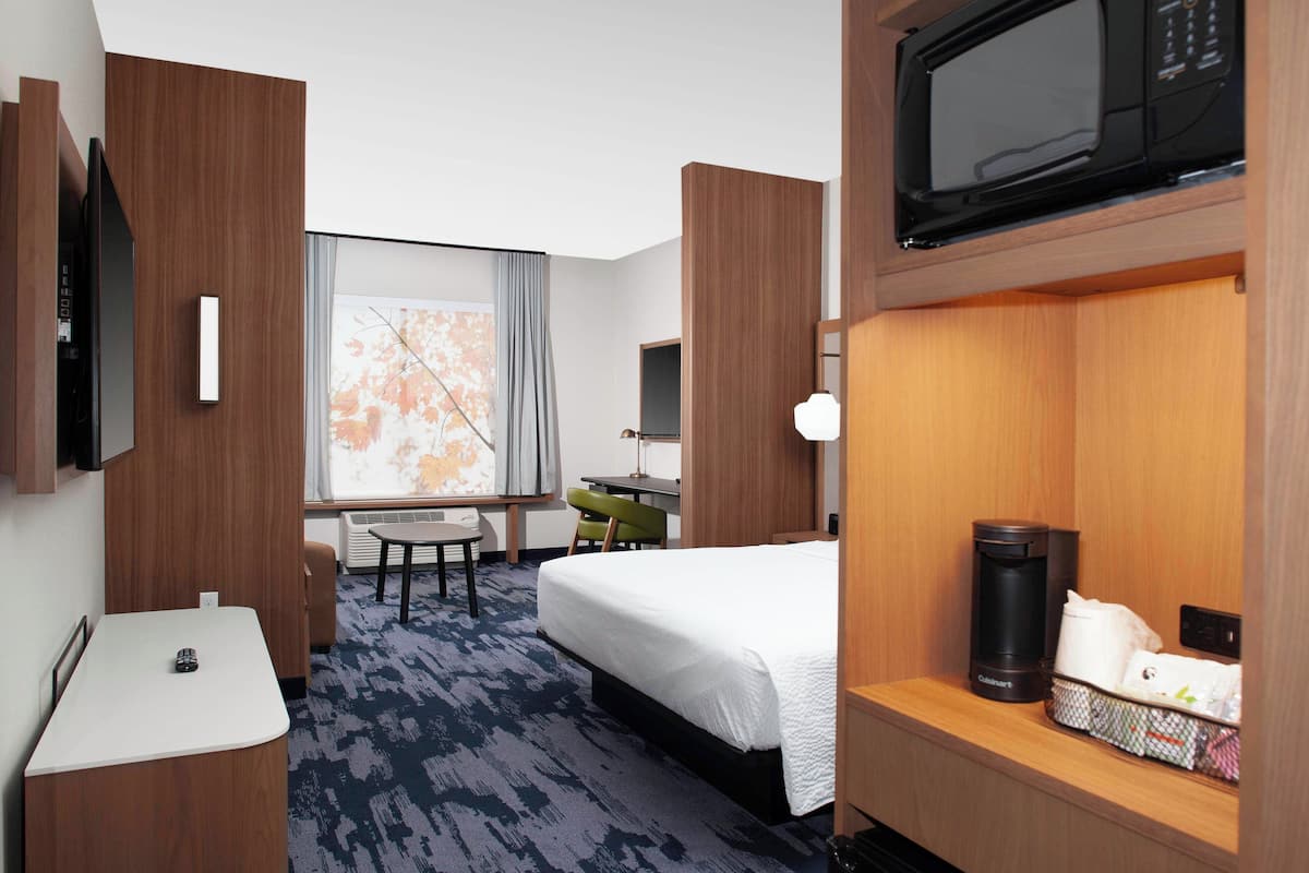 A hotel room with a bed, a desk, a chair, a microwave, and a coffee maker.