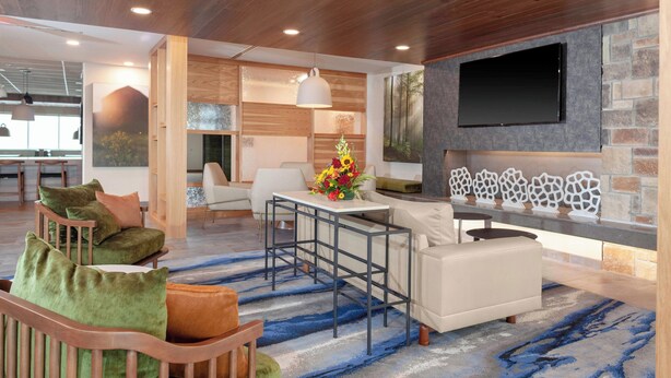 A modern living room with a sofa, chairs, a coffee table, and a TV mounted on a stone wall. - Fairfield Inn & Suites by Marriott Fort Morgan (Fort Morgan)