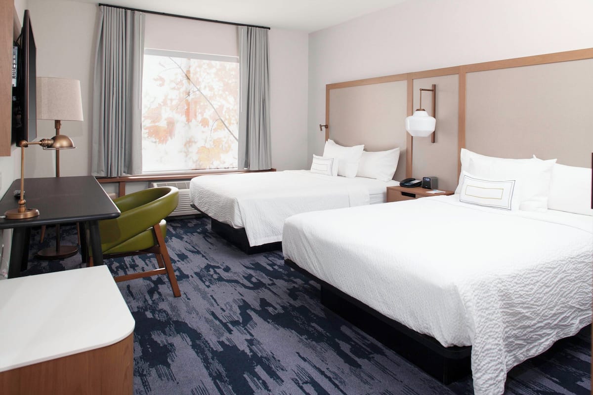 A hotel room with two beds, a desk, a chair, and a large window with curtains.