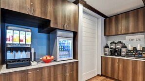 Una cocina con refrigerador, cafetera y un letrero que dice “On Us”.