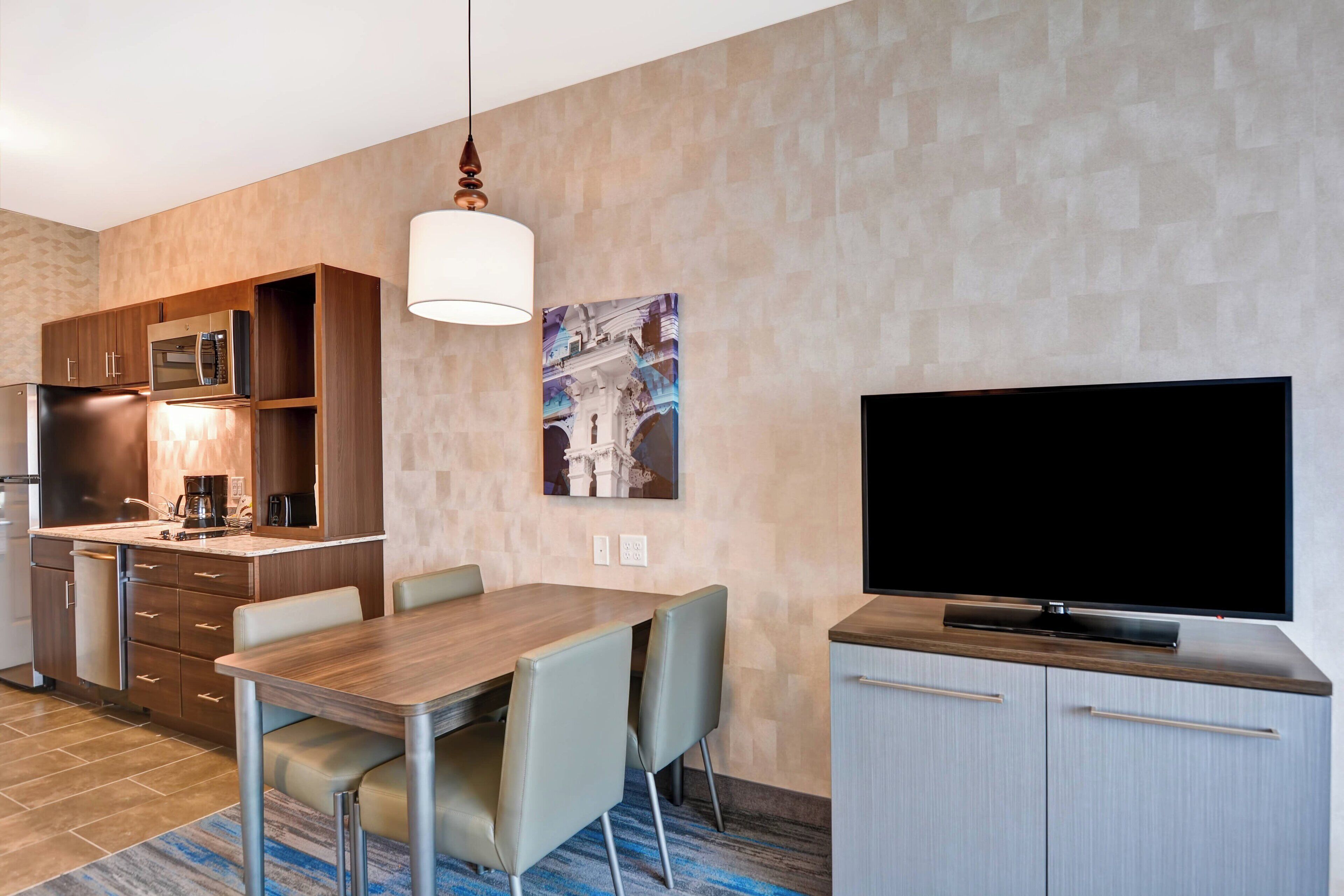 Une chambre d’hôtel moderne dotée d’un coin repas, d’une kitchenette et d’un téléviseur à écran plat.