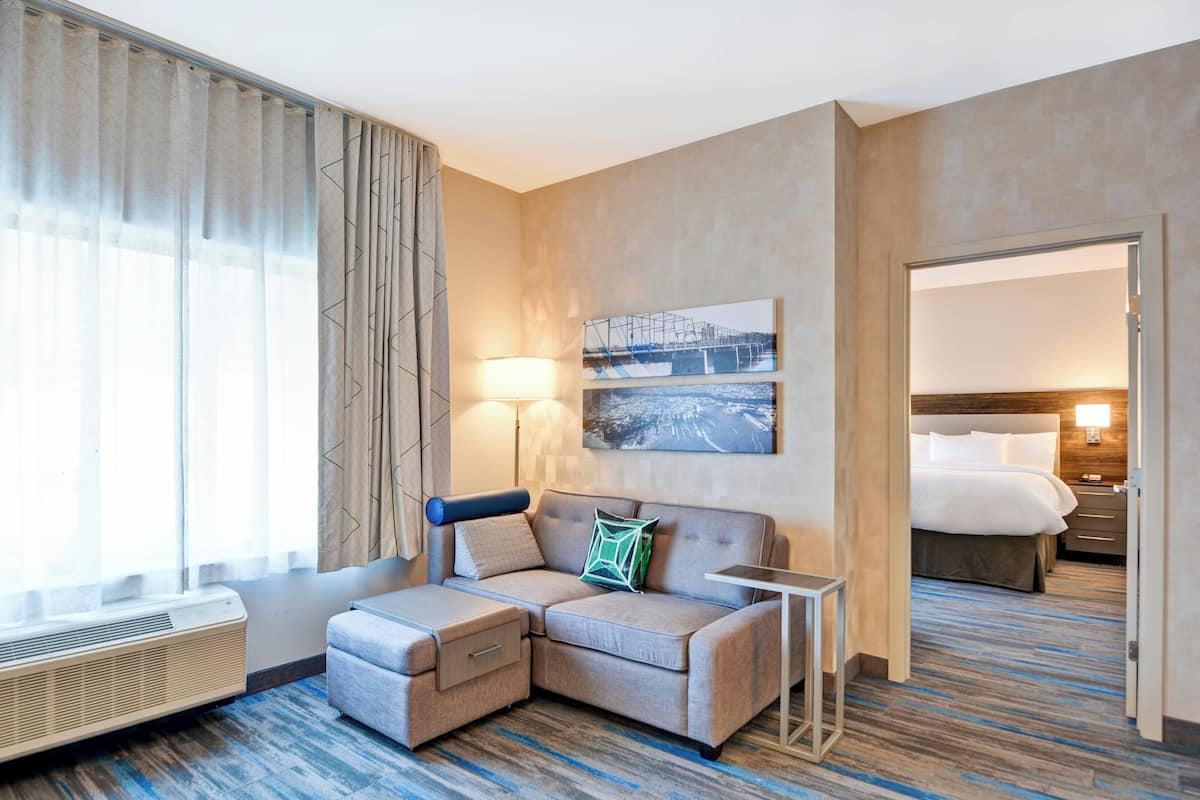 A hotel room with a sectional sofa, a small table, a bed, and a wall-mounted picture.
