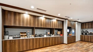 Una cocina moderna con armarios de madera, una encimera con diversos electrodomésticos y suelo de baldosas.