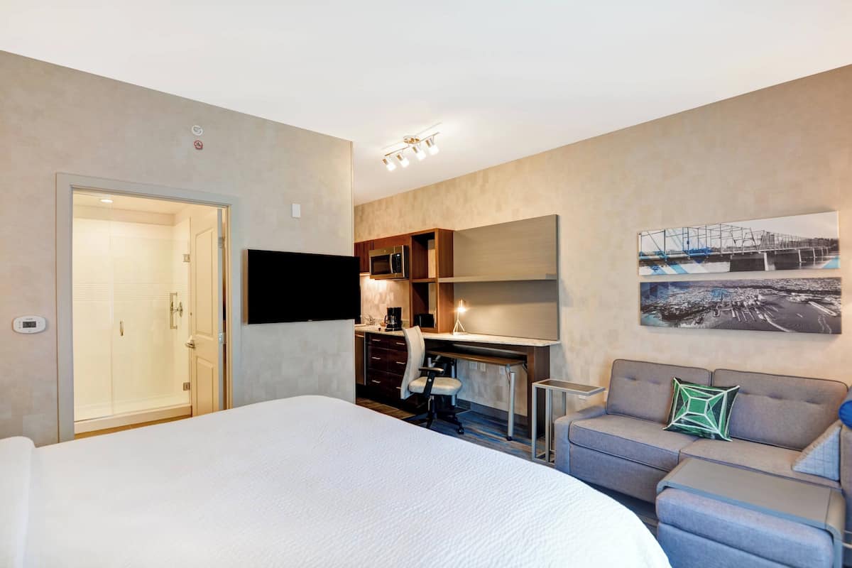 A hotel room with a large bed, a desk with a chair, a sofa, a flat-screen TV, and a picture on the wall.