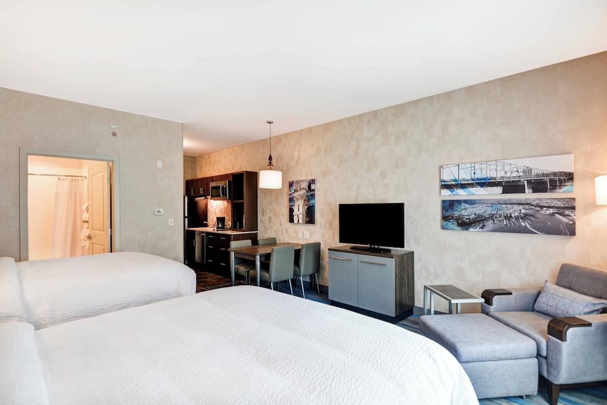 A hotel room with a large bed, a desk with a TV, a sofa, and a dining area.