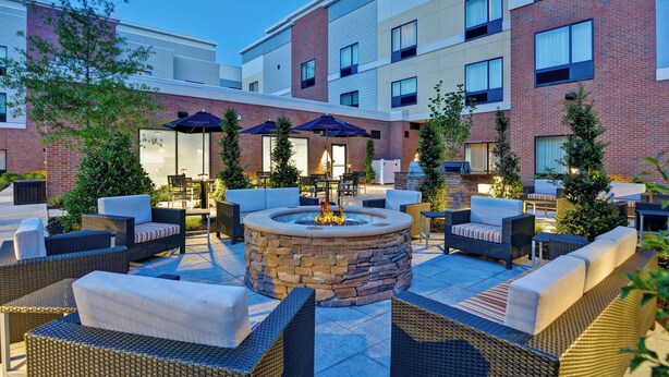 Un patio con mobiliario exterior, una chimenea y un edificio con varias ventanas y balcones.