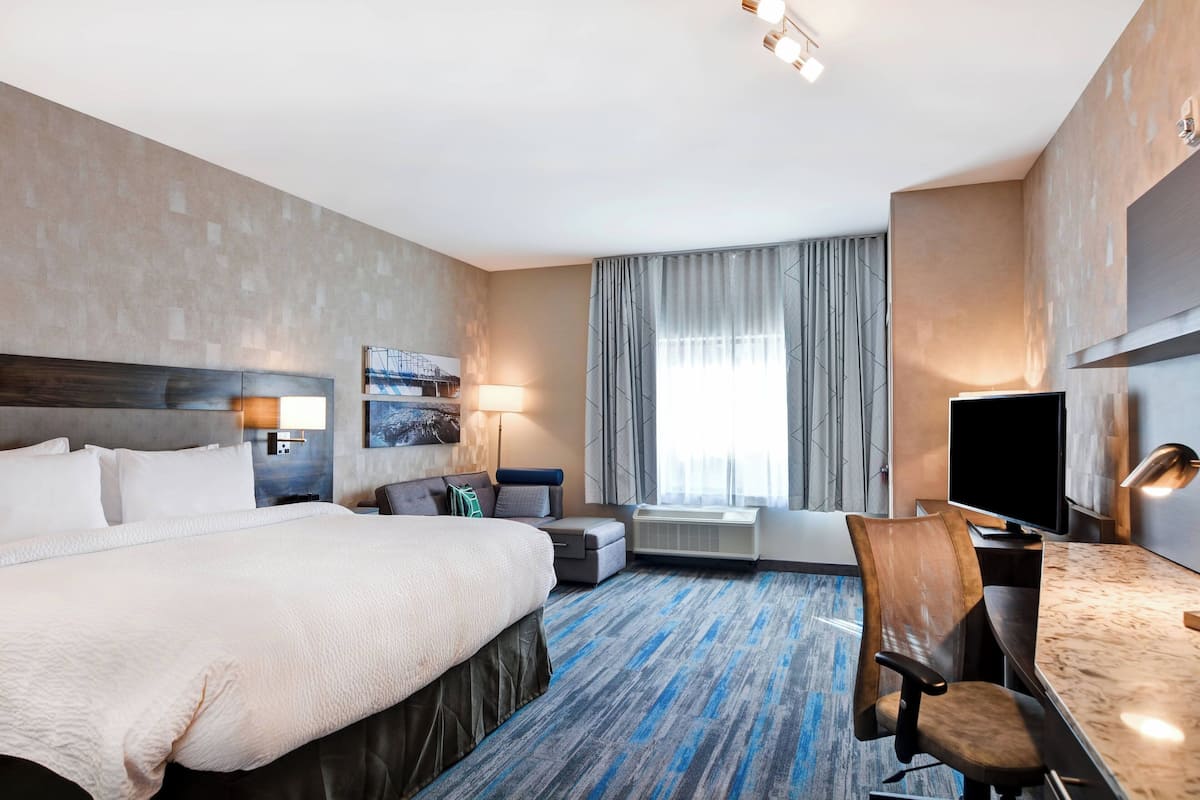 A hotel room with a large bed, a desk with a chair, a television, and a window with curtains.