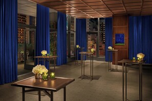 Vestíbulo de hotel con cortinas azules, paneles de madera y varias mesas con arreglos florales.