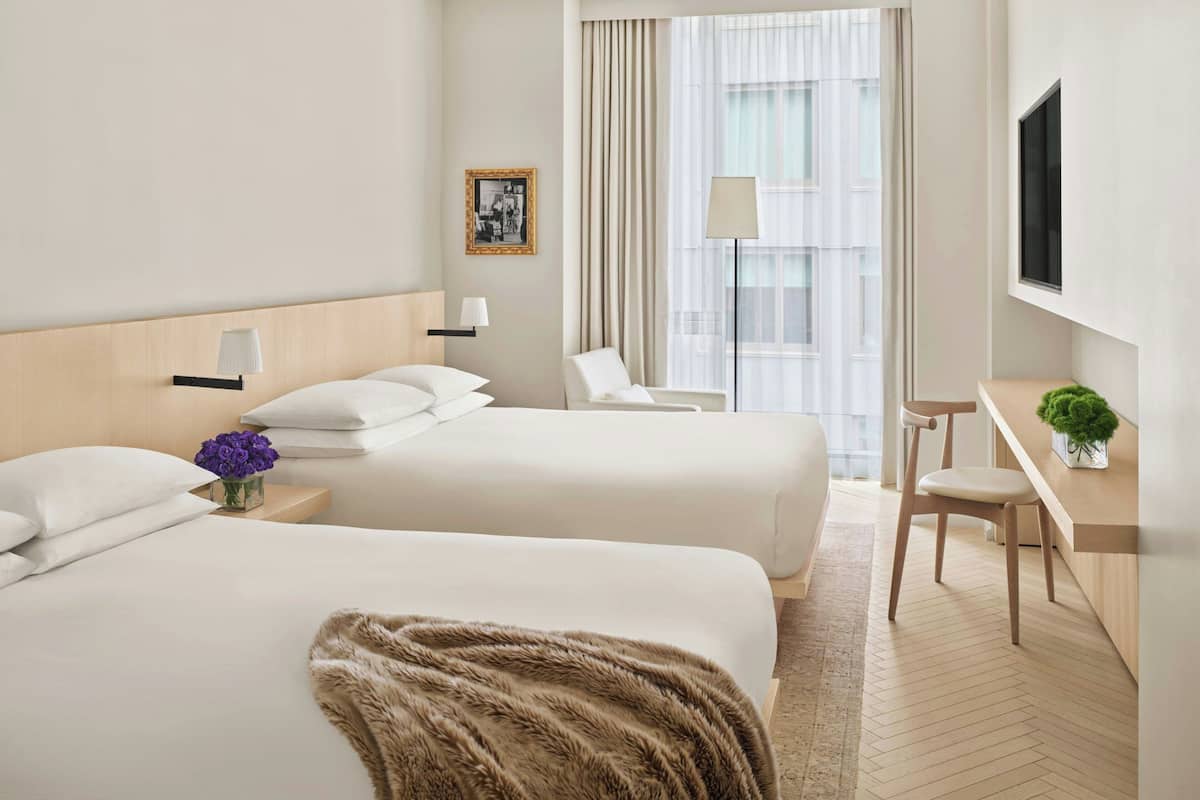 Une chambre d’hôtel avec deux lits, un bureau, une chaise, une télévision et une fenêtre avec des rideaux.