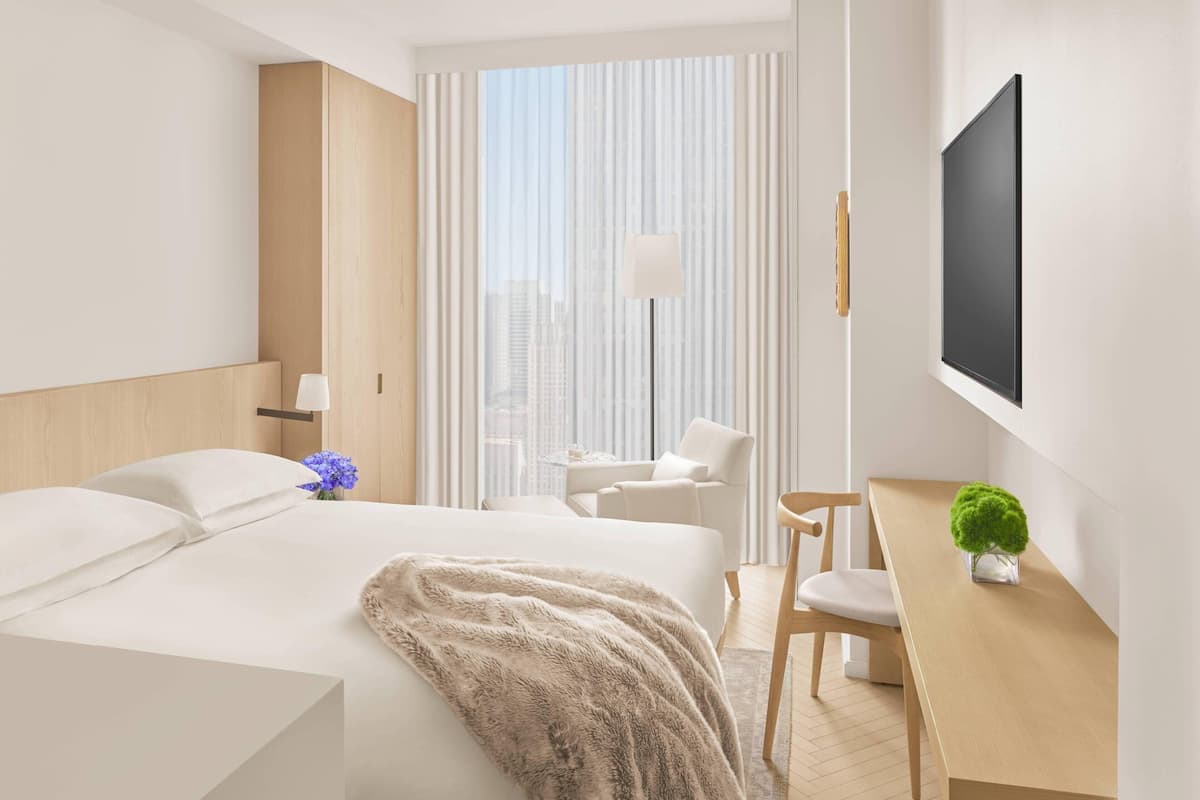Une chambre d’hôtel moderne dotée d’un grand lit, d’un bureau, d’une chaise, d’une télévision et offrant une vue sur la ville grâce à de grandes fenêtres.