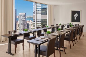 A conference room with a long table, multiple chairs, and a city view through large windows.