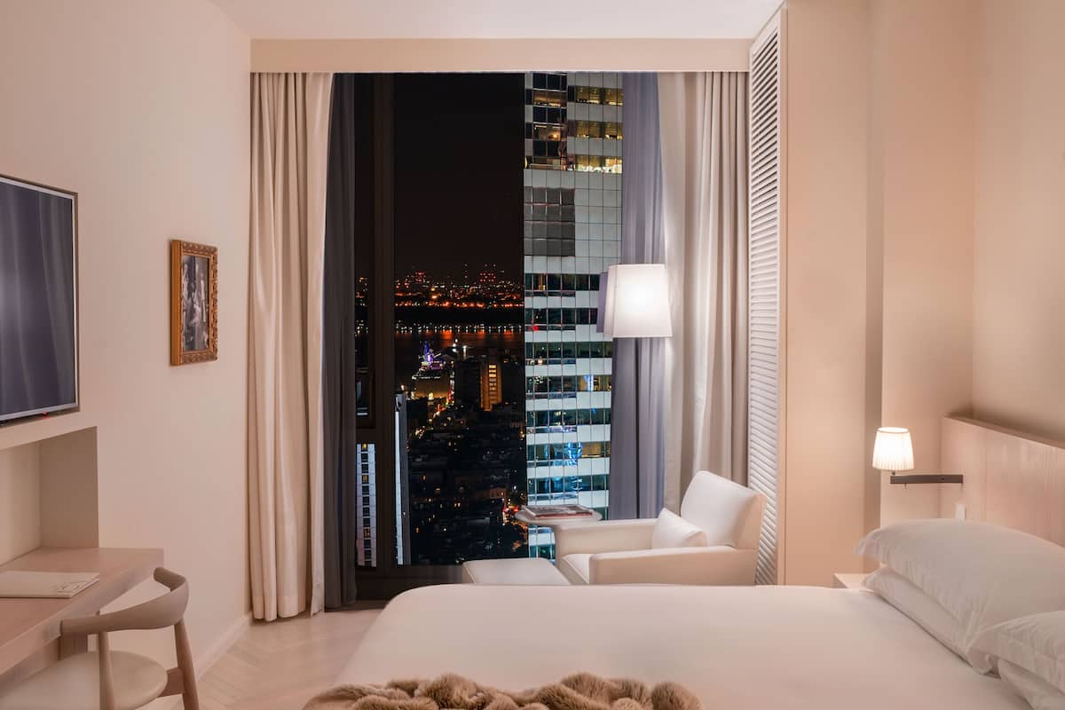 Une chambre d’hôtel moderne avec un grand lit, un bureau et une vue sur le paysage urbain.