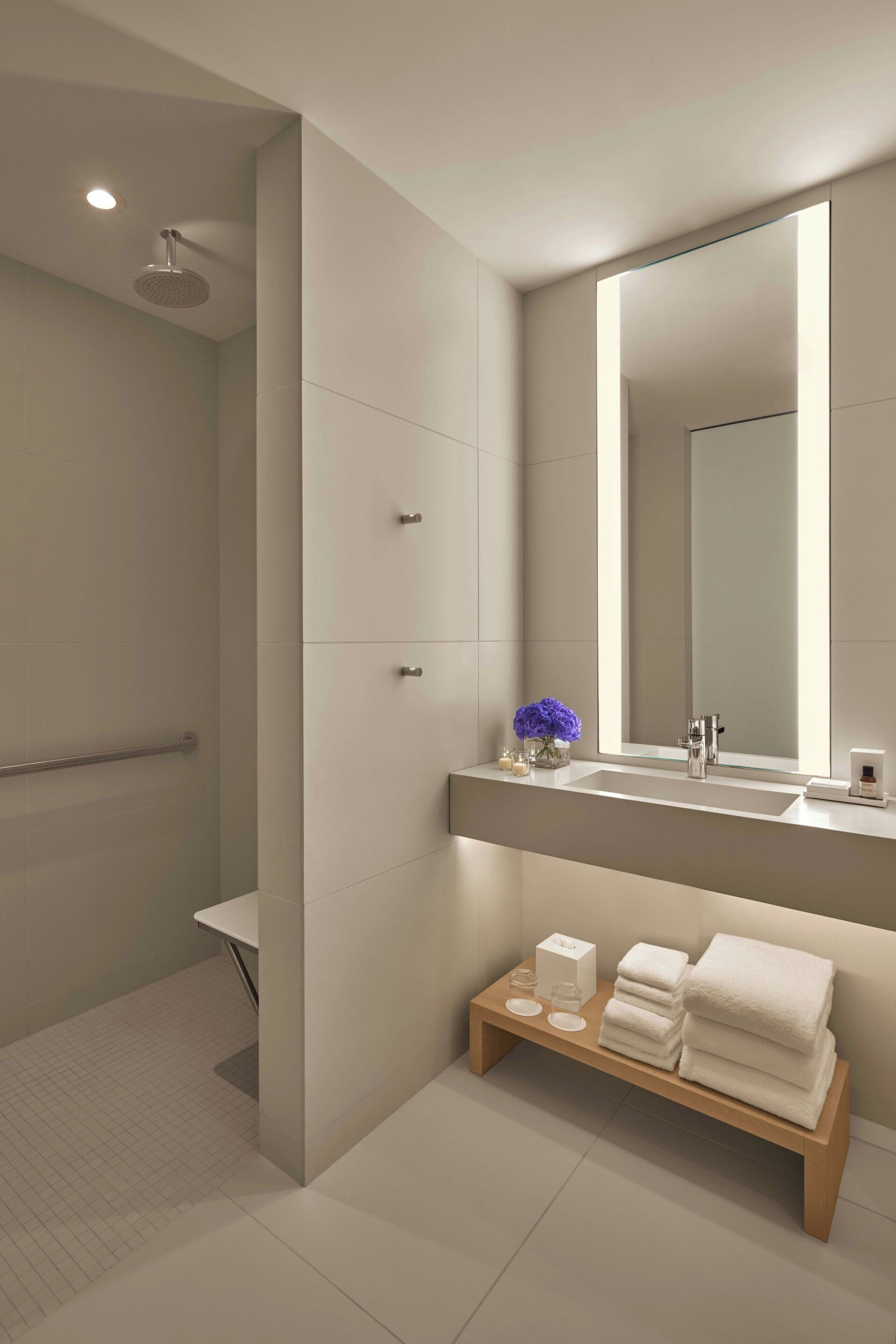 Une salle de bain moderne avec un grand miroir, une douche et un meuble-lavabo doté d’un évier et d’un porte-serviettes.