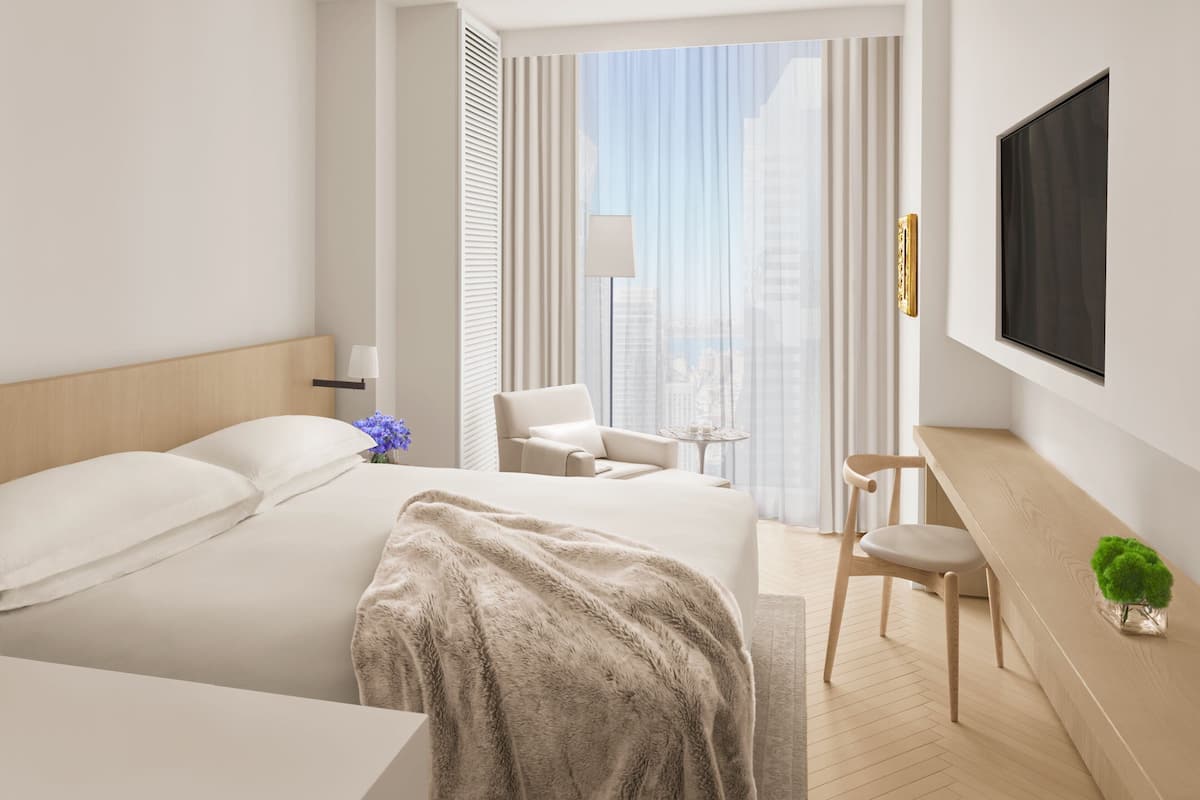 Une chambre d’hôtel avec un lit, un bureau, une chaise, une télévision et une vue sur la ville.