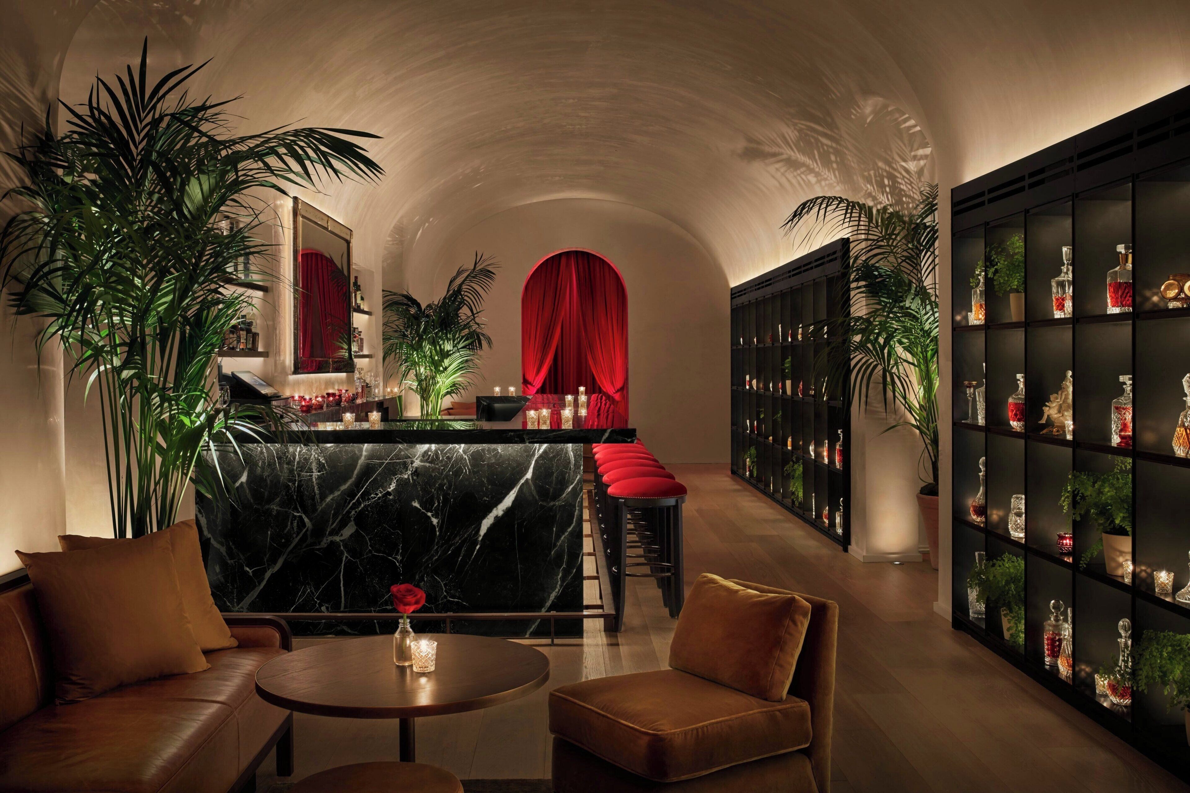 Un intérieur luxueux avec un bar en marbre, des rideaux rouges et une bibliothèque remplie d’objets décoratifs.