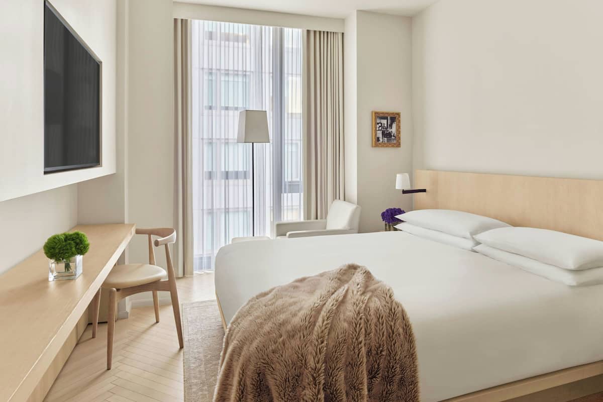 Une chambre d’hôtel avec un lit, un bureau, une chaise, une télévision et une fenêtre avec des rideaux.