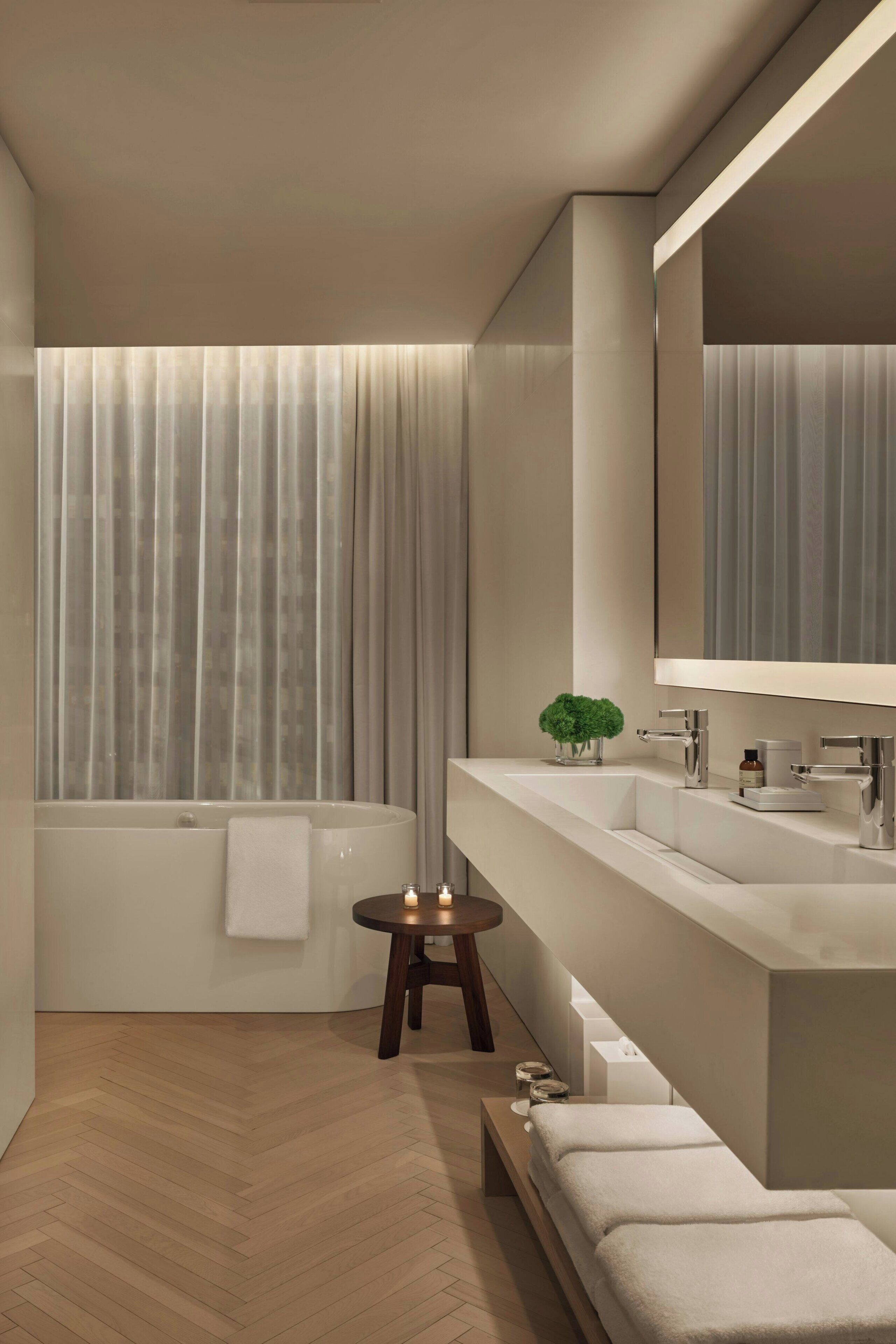 Ein modernes Badezimmer mit einer Badewanne, zwei Waschbecken, einem großen Spiegel und einem kleinen Tisch mit einer Pflanze.