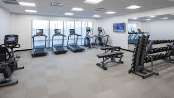 A gym with treadmills, elliptical machines, a bench press, and a rack of dumbbells.