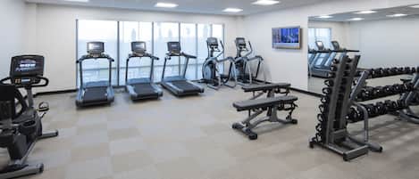A gym with treadmills, elliptical machines, a bench press, and a rack of dumbbells.