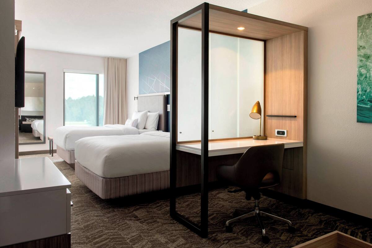 Habitación de hotel con dos camas, un escritorio, una silla, un televisor y una ventana.