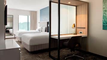 A hotel room with two beds, a desk, a chair, a TV, and a window.