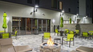Un patio al aire libre con suelo de piedra, sillas verdes y una chimenea central.