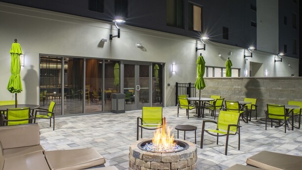 Un patio al aire libre con suelo de piedra, sillas verdes y una chimenea central.
