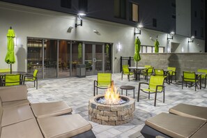 An outdoor patio with stone flooring, green chairs, and a central fire pit. - SpringHill Suites by Marriott Tampa Suncoast Parkway (Land O' Lakes)