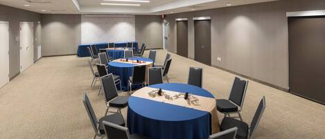 A conference room with round tables, chairs, and a carpeted floor.