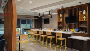 Un área de bar moderna con una barra larga, varios taburetes y un televisor montado en la pared.