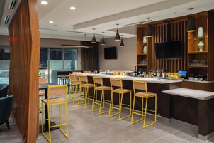 Un área de bar moderna con una barra larga, varios taburetes y un televisor montado en la pared.