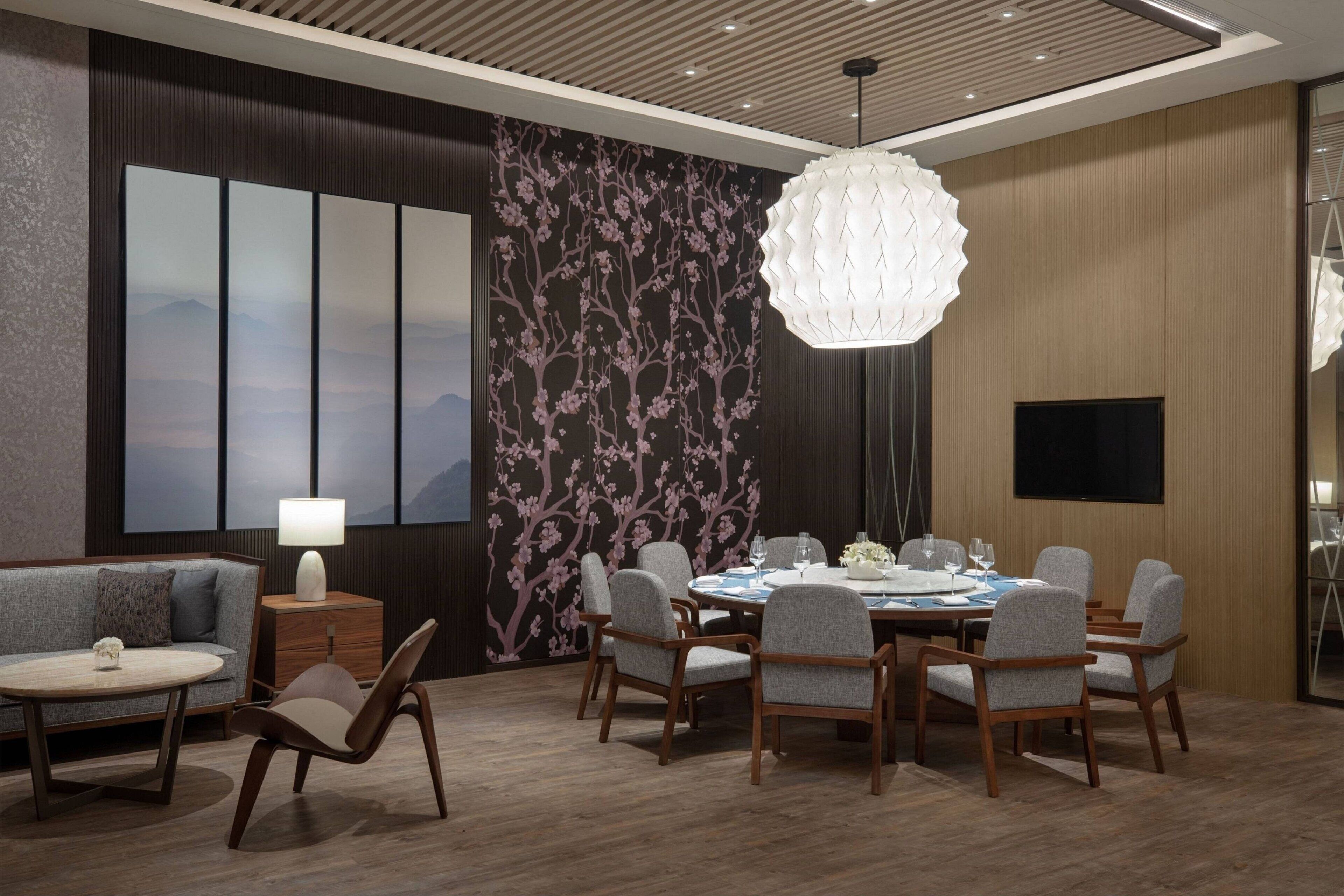 Een moderne eetruimte met een ronde tafel, zes stoelen, een bank, een lamp en een decoratieve wand met een bloemmotief.