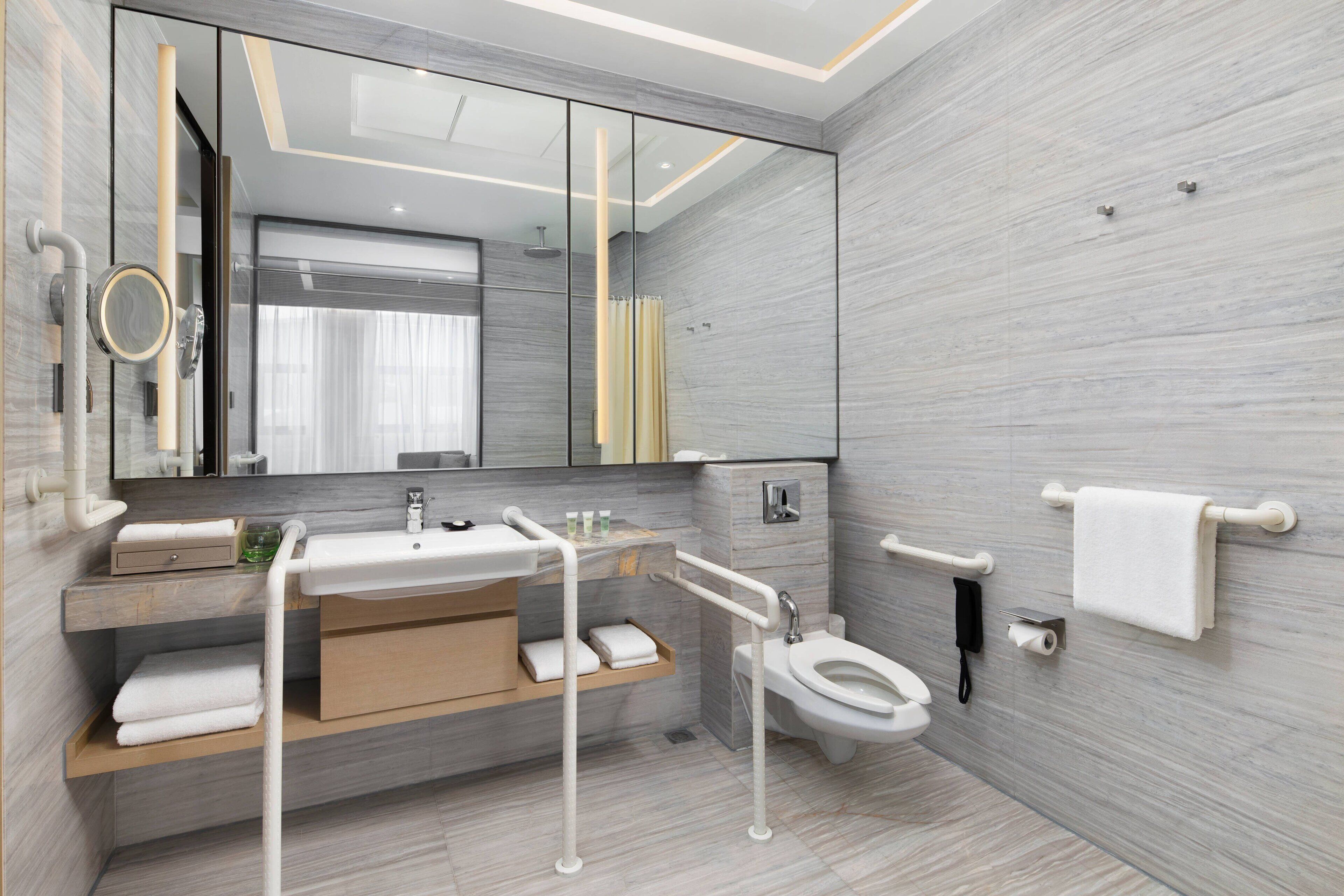 A modern bathroom with a large mirror, a sink, a toilet, and a shower area.